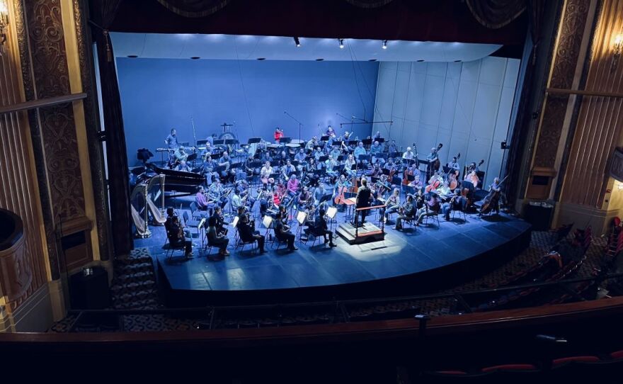 Picture from the balcony is an historic theatre with a symphony on the stage.