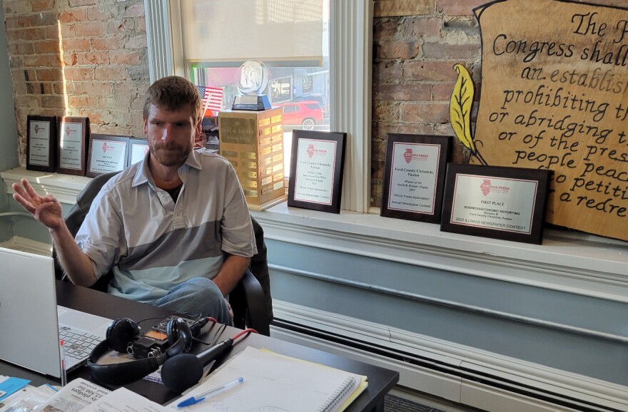 News editor and co-publisher Will Brumleve sits at his desk at the Ford County Chronicle in front of awards and text from the First Amendment. He and co-founder Andrew Rosten launched the newspaper in Paxton, Illinois, in 2020, one of the few new papers in the U.S. in recent years.