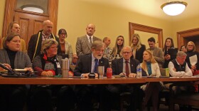 Sen. Herman Quirmbach, D-Ames, speaks against Gov. Kim Reynolds school choice bill flanked by fellow lawmakers in a crowded hearing room.