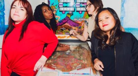 Four women who make up the band Big Salt stand around a pin ball machine. 