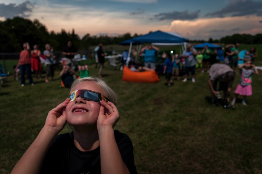 In this file photo from Aug. 21, 2017, Clarey Huck was peering through her eclipse glasses just before totality in De Soto, Missouri. Several towns within the path of the coming total eclipse on April 8 are preparing for thousands of visitors.