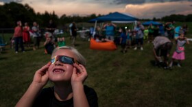 In this file photo from Aug. 21, 2017, Clarey Huck was peering through her eclipse glasses just before totality in De Soto, Missouri. Several towns within the path of the coming total eclipse April 8 are preparing for thousands of visitors.