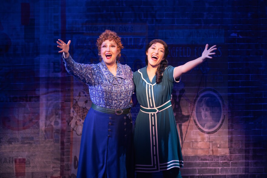 Two women sing on stage with their hands outstretched towards the audience.