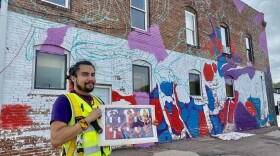 David Manzanares stands in front of his half finished mural in Sioux City. He holds the planned finished design.