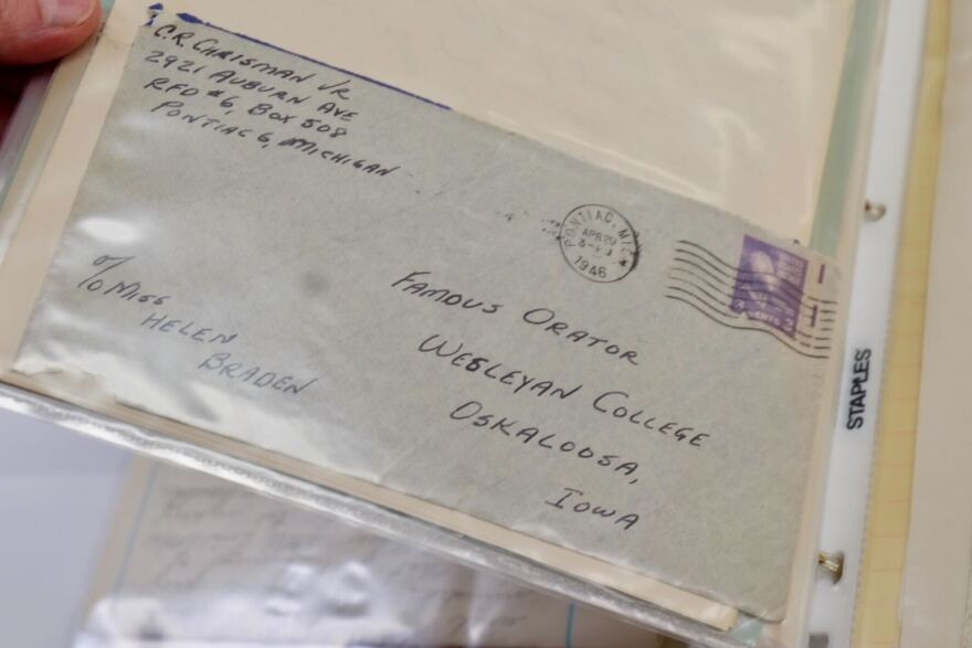 A handwritten letter from the 1940s is held, wrapped in a plastic covering. 