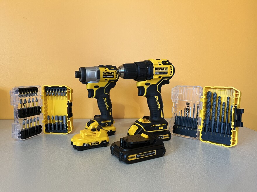 A cordless drill and impact driver sit on a table with drillbits