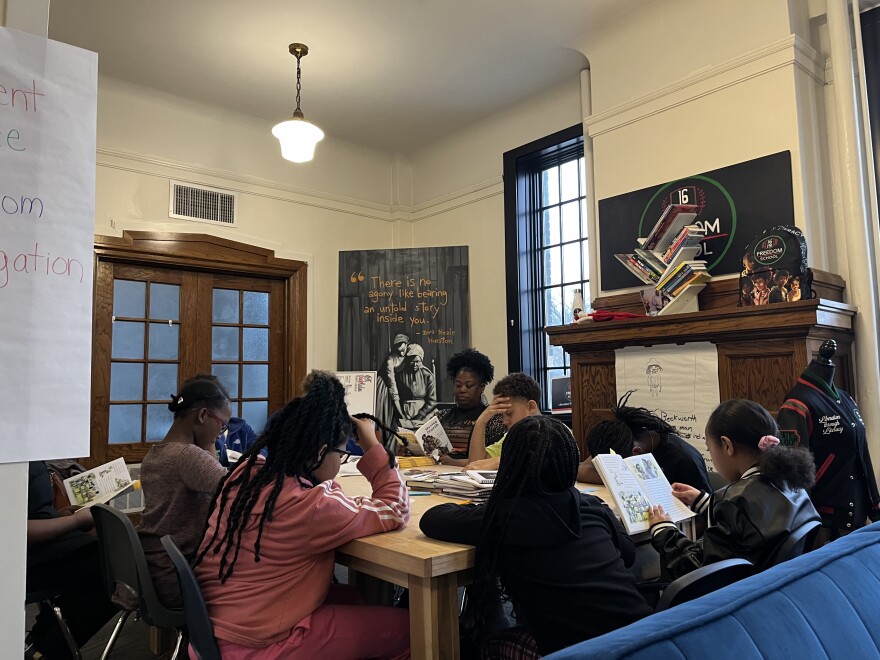 Six kids and one teacher at a table reading books.