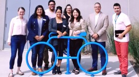 Eight commissioners pose for a picture in front of a blue bike sculpture.