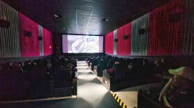 A movie theater auditorium is full of people watching a movie on the big screen