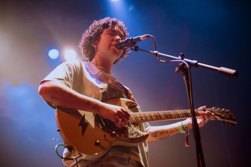 Light at her back, a guitarist sings into a microphone.