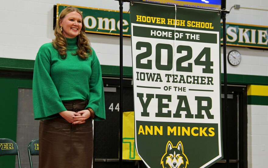 2024 Iowa Teacher of the Year Ann Mincks stands with a banner that will hang in Hoover High School.