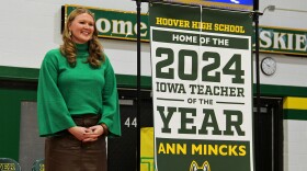 2024 Iowa Teacher of the Year Ann Mincks stands with a banner that will hang in Hoover High School.