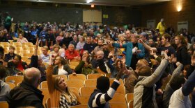 People in a crowd in an auditorium raise their hands to be counted on caucus night 2020. 