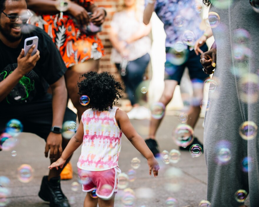  A child surrounded by bubbles dances in the pocket park at 80/35. 