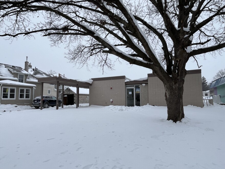 Gray brick building with large tree in front in snow.