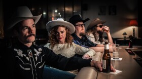 A color image of Katie and the Honky Tonks at a bar. Katie is facing the camera, while the others are looking over the bar.  