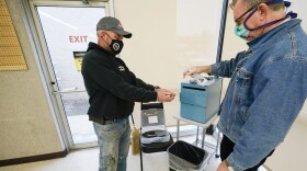 Chris Helps, of Earlham, Iowa, gets his hands sanitized by polling place volunteer Frank Hayer, right, during early voting, Tuesday, Oct. 20, 2020, in Adel, Iowa.