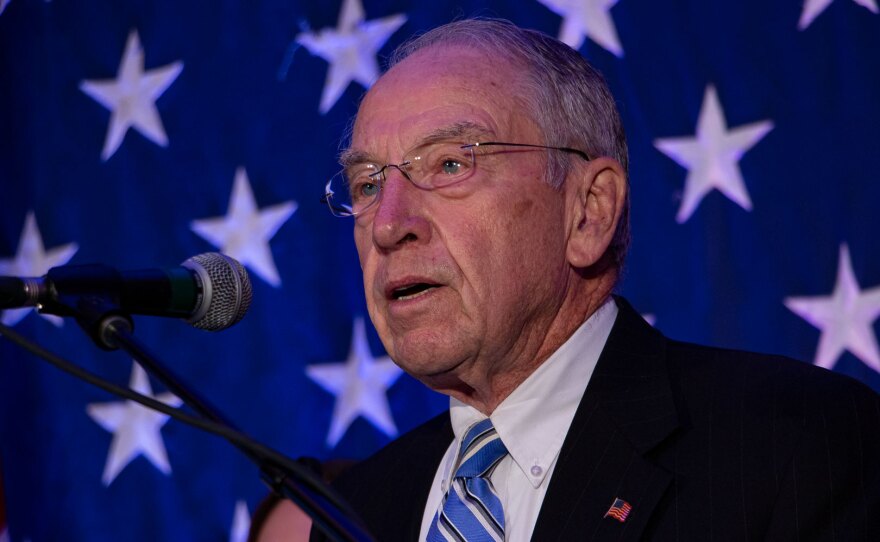 Sen. Grassley speaks into a microphone in front of an American flag.