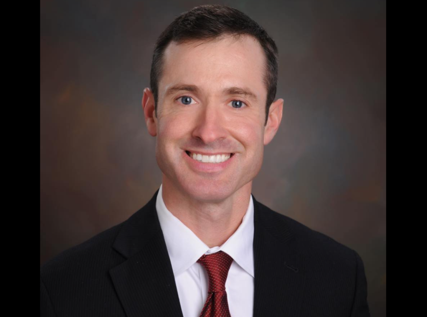 Man wearing a suit and red tie with a white shirt is smiling. 