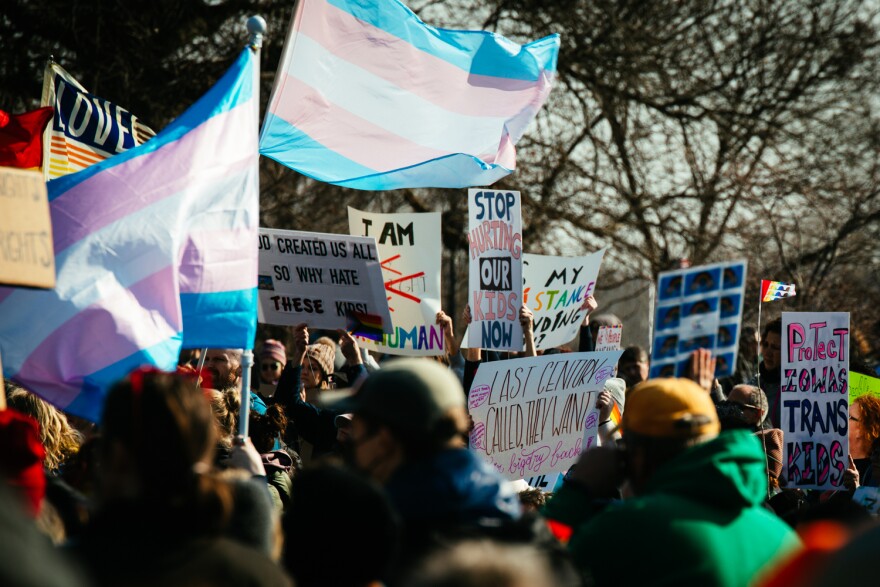 protesters hold signs and flags in support of transgender Iowans