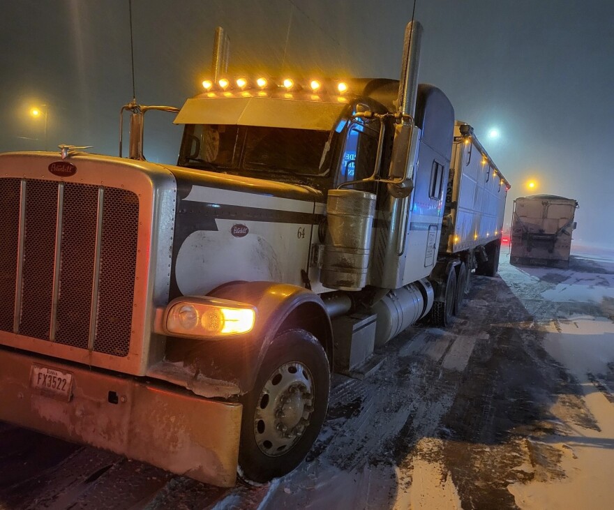 A semi truck is parked in a parking lot with a bit of snow on the ground.