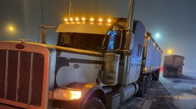 A semi truck is parked in a parking lot with a bit of snow on the ground.