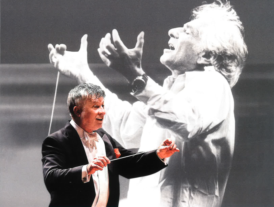 A symphony conductor holds out a baton against a backdrop of Leonard Bernstein conducting.