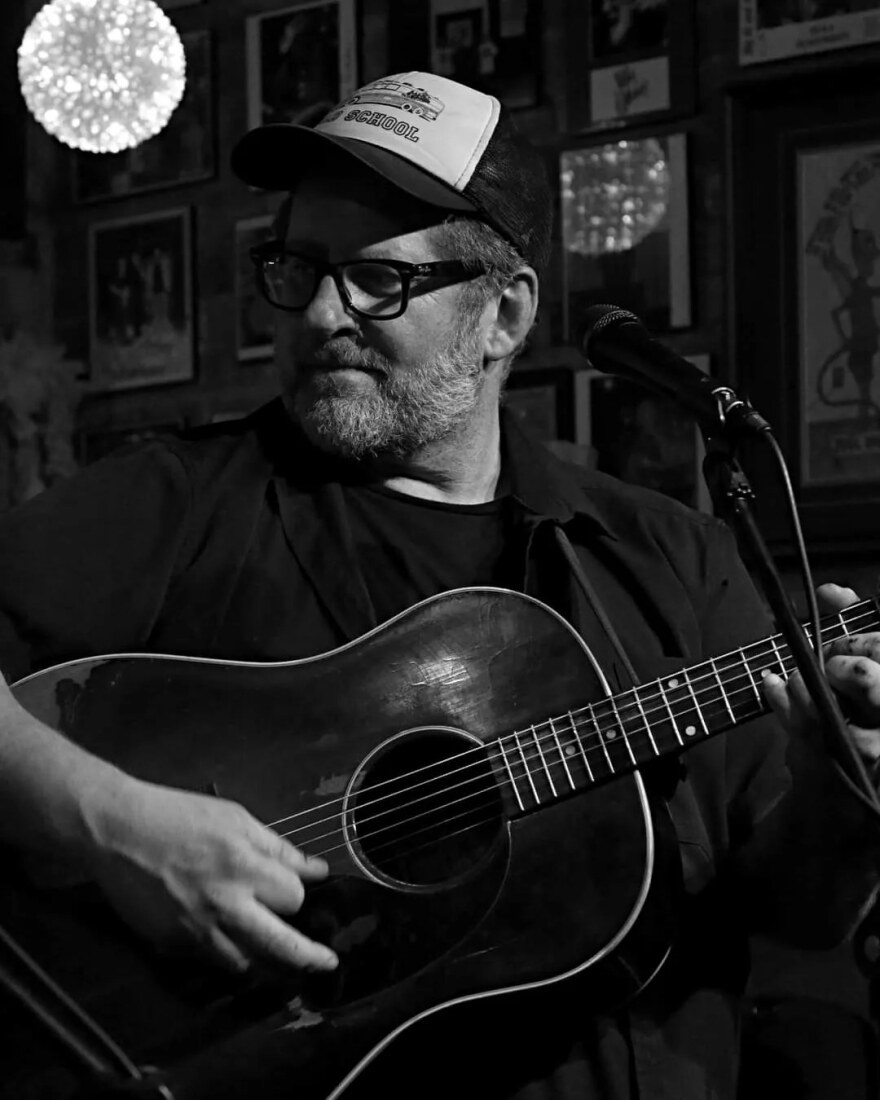 a black and white photo of a man holding an acoustic guitar as he looks over his shoulder