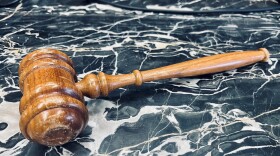 Brown gavel is on a gray and white swirled marble countertop.