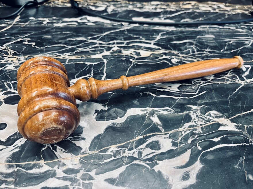 Brown gavel is on a gray and white swirled marble countertop.