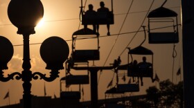 A perspective photo of the state fair sky chair at sunset. A lampost is in the foreground with the sun setting behind it. 