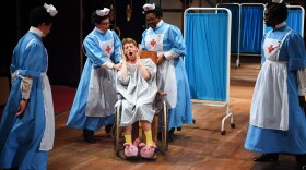 man in a wheelchair surrounded by doctors on an opera stage