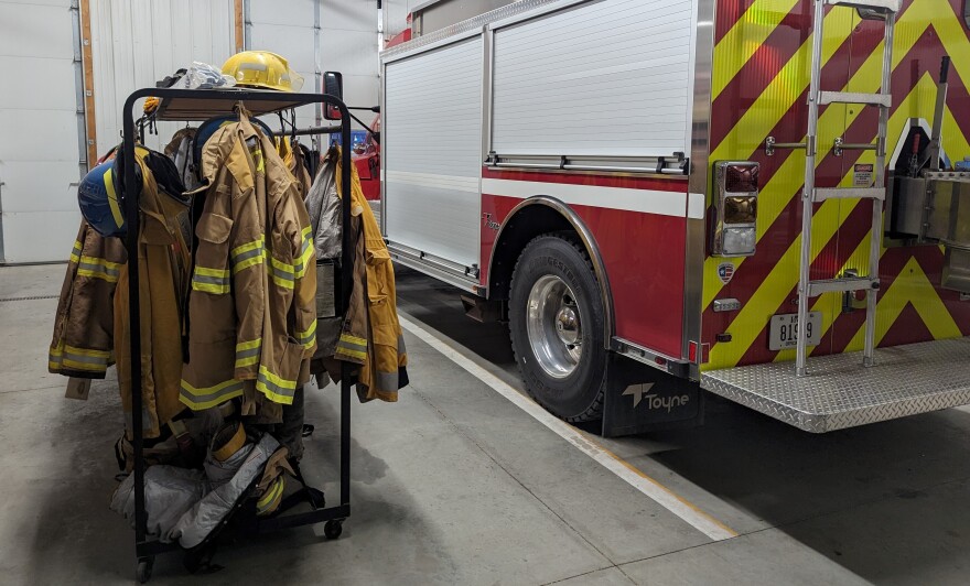 Picture of inside a fire station with uniforms to the left and a fire truck to the right.