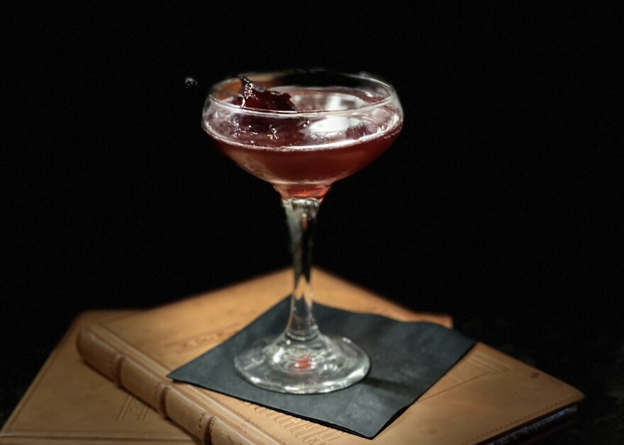 The Other Room's Mumbai Expedition is a gin-forward cocktail with violet liqueur, Bombay East gin, lemon, hibiscus cubeb and a green chartreuse glaze. It is garnished with a candied hibiscus flower. 