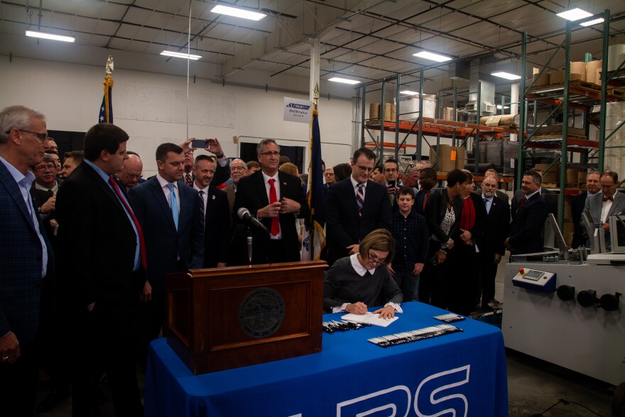 Kim Reynolds signs a bill while lawmakers watch. 