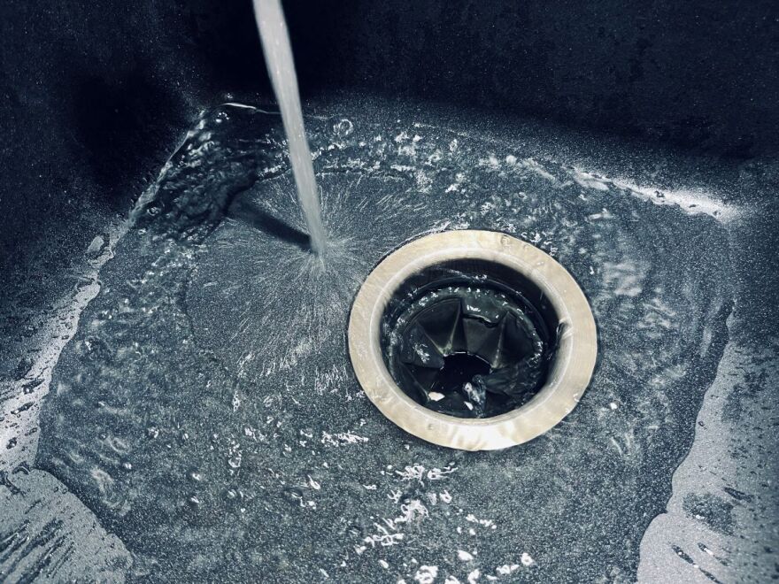 A stream of water is pouring into a dark grey sink.