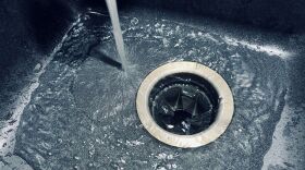 A stream of water is pouring into a dark grey sink.