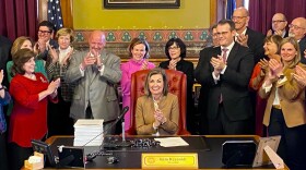 governor kim reynolds and other government officials clap their hands after she signed a bill 